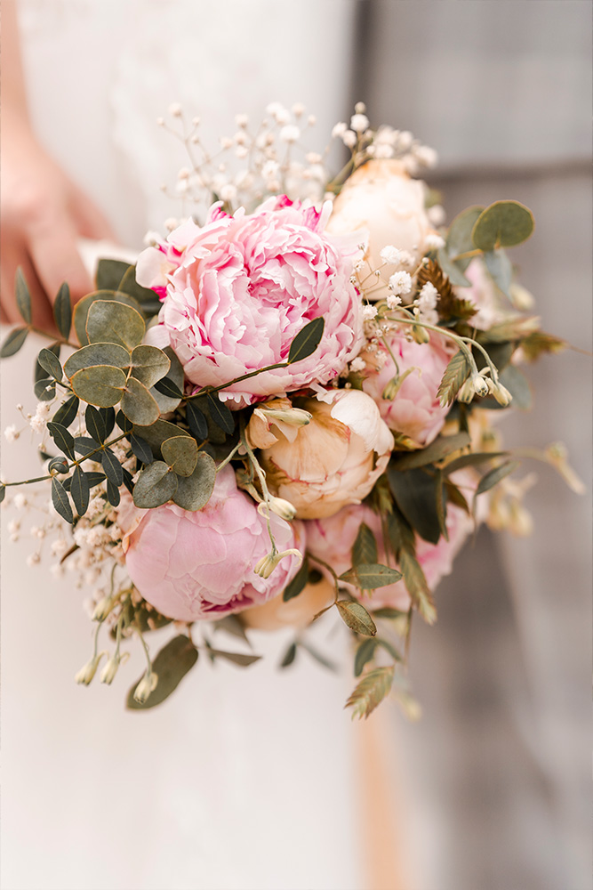 Een prachtig bruidsboeket met een mix van bloemen in zachte pasteltinten, waaronder rozen, lelies en baby's adem. Het boeket is elegant gebonden met een lint en straalt romantiek en verfijning uit, perfect voor een bruiloft